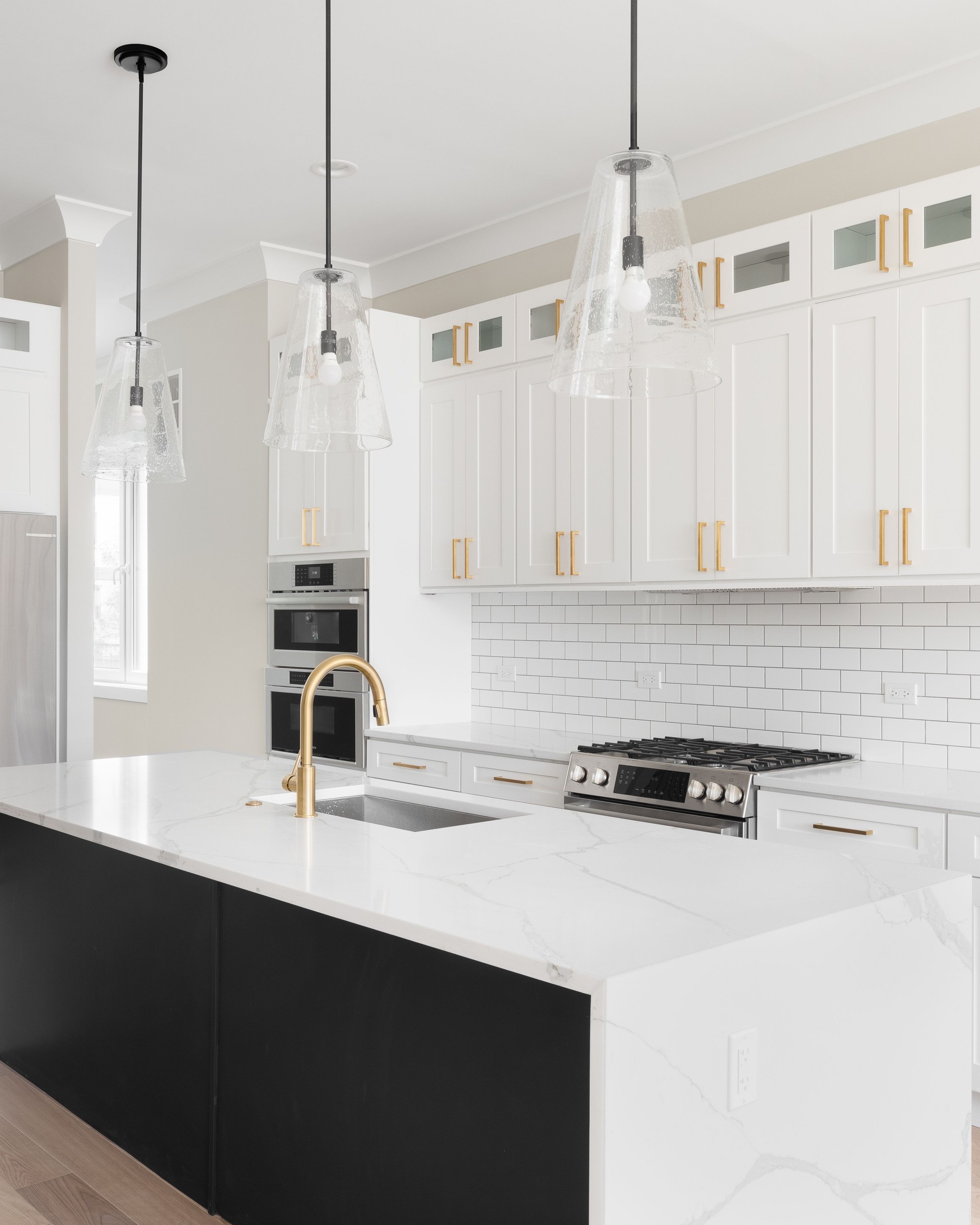 A white and black kitchen with lights hanging above the waterfall granite island.